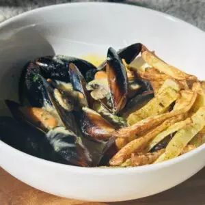 Bowl of mussels in creamy sauce with crispy fries on a wooden table. Perfect seafood dish for a tasty meal.